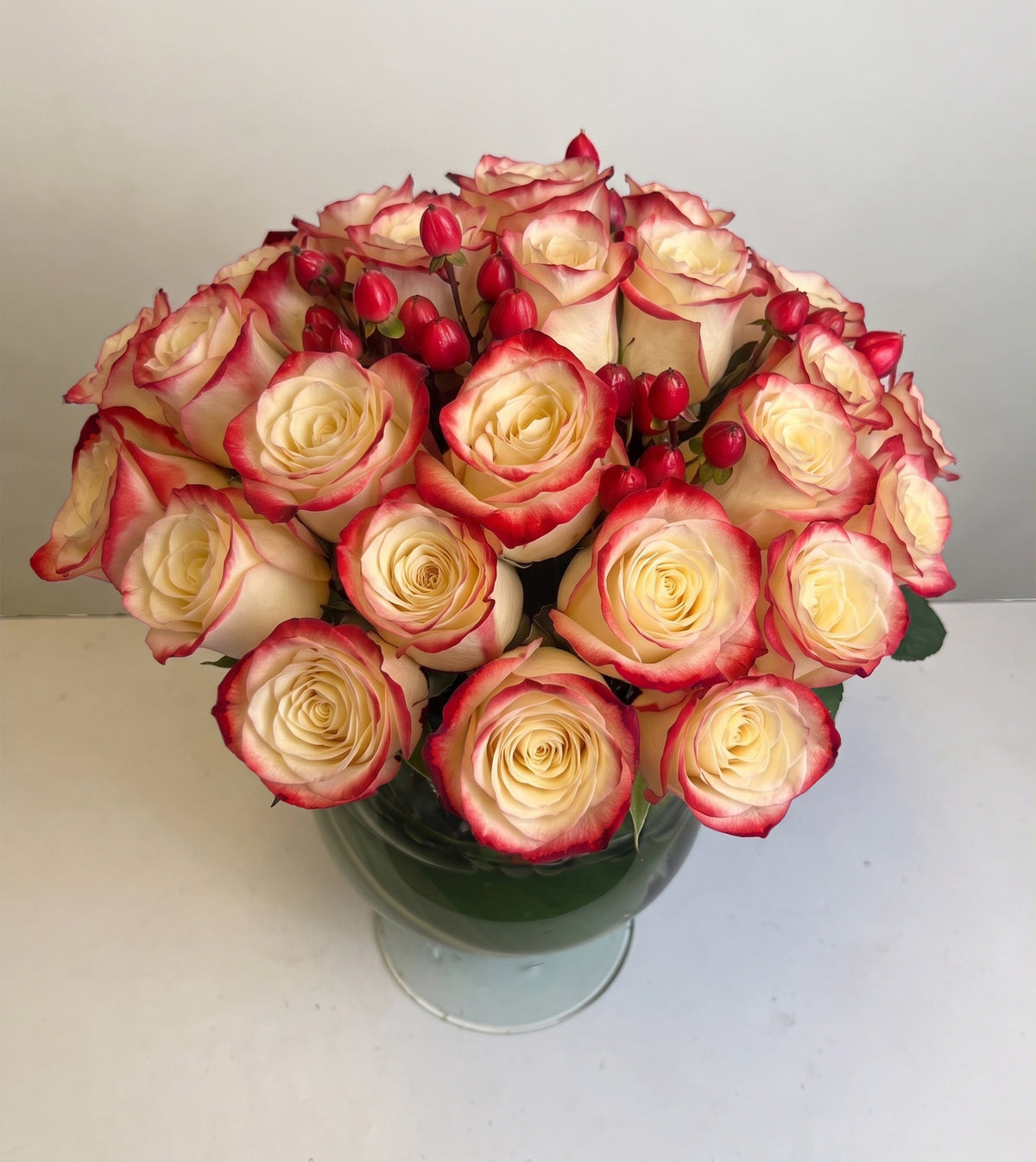 Arreglo con 30 rosas e hiperycum en florero copón, rosas blush (crema con borde rojo)