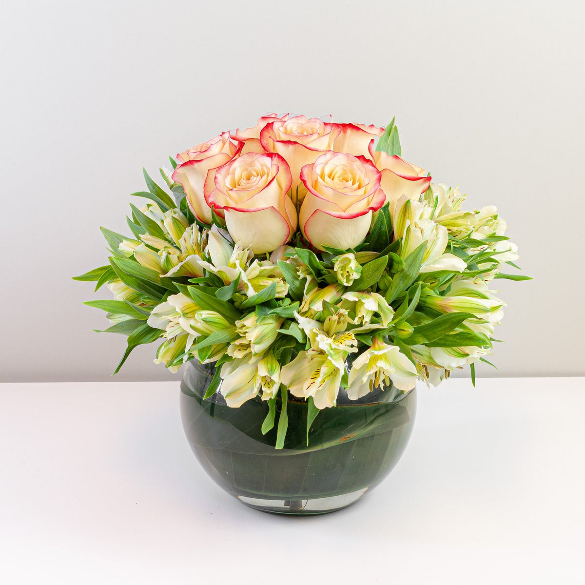 Arreglo con 7 rosas y astromelias en pecera mediana, rosas blush (crema con borde rojo)